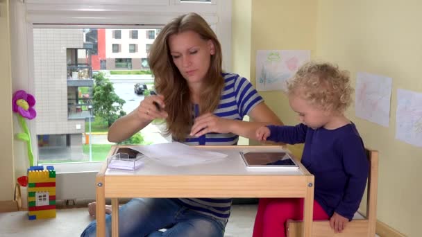 Freelancer vrouw maken telefoontje en haar peuter dochter spelen met tablet — Stockvideo