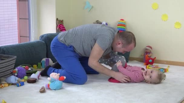 Happy young father tickle toddler daughter on carpet between toys at home. — Stock Video