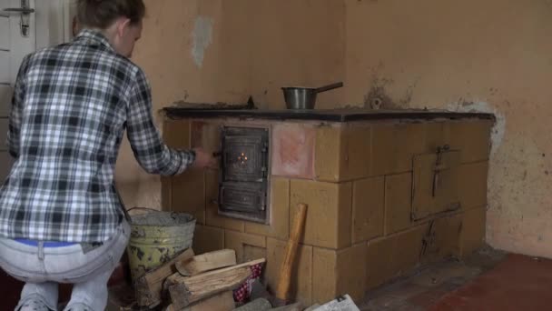 Κορίτσι βάλει ξύλο σε παλιά ρουστίκ πηλό φούρνο στην κουζίνα εξοχικό. 4k — Αρχείο Βίντεο