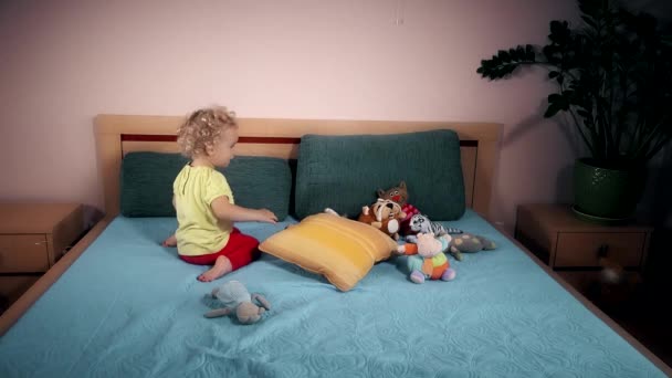 Niño travieso lanzando juguetes en la cama en el dormitorio . — Vídeos de Stock