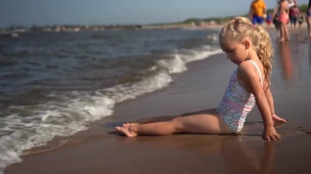 Cute little girl sitting on coastline and meeting waves on shore. Child run away — Stock Video