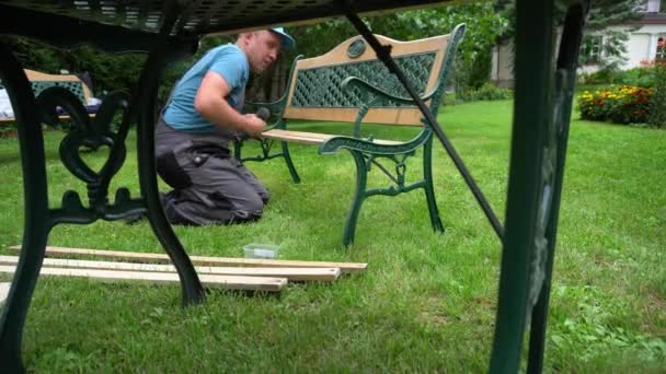 Ouvrier homme démonter banc rétro en pièces. Processus de renouvellement des meubles d'extérieur — Video