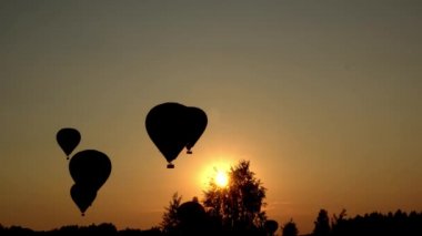 Hot air balloons landing over amazing sunset. Sunbeams penetrate through trees