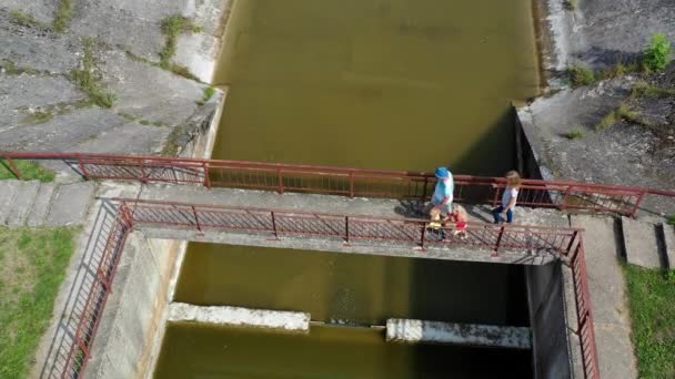 Adultos e crianças viajam. Família caminhando na velha ponte da barragem abandonada — Vídeo de Stock