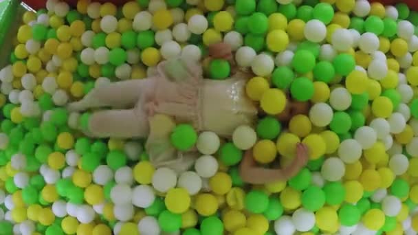 Actief meisje in roze jurk spelen in speeltuin vol plastic kleurrijke ballen — Stockvideo