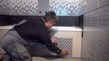 Becerikli adam banyo küvetinin kenarına fayanslar döşedi.