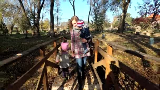 Mère avec deux petits enfants marchant sur un pont en bois recouvert de feuilles d'automne — Video