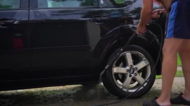 İşçi siyah otomobili yüksek basınçlı su ekipmanıyla yıkıyor.