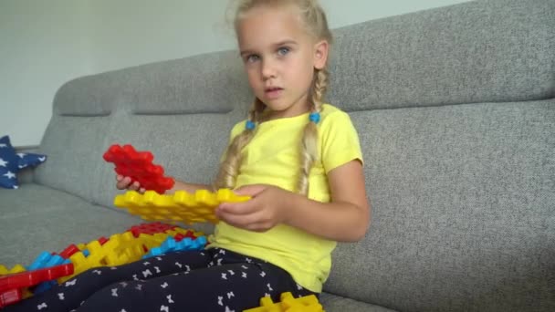 En liten flicka som kopplar ihop delar som sitter på soffan. Gimbal rörelse — Stockvideo