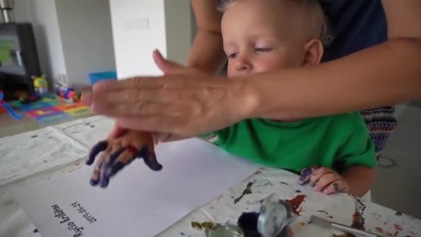 Frau mit kleinem Jungen fertigt Handabdruck-Stempel mit Gouachefarbe — Stockvideo