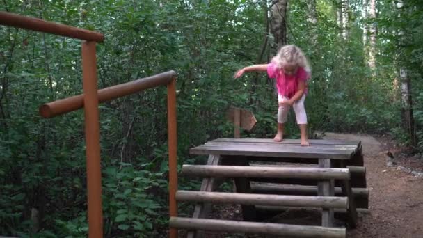 Boso-noga dziewczynka przechadza się po drewnianym moście. Ścieżka do masażu stóp — Wideo stockowe