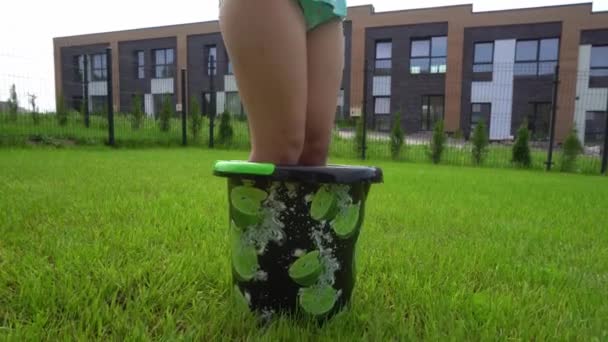 Söt flicka i baddräkt med leksak vatten pistol i händerna stående i vatten hink — Stockvideo