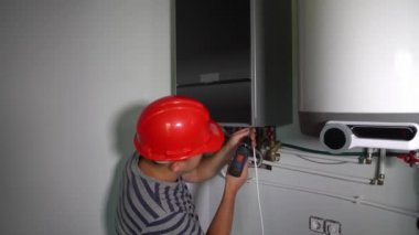 Elektrikli tornavidayla inşaat işçisi ön panel gaz kazanını takıyor.