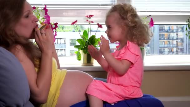 Pregnant woman playing with mouth organ and cute little daughter clap hands — Stockvideo