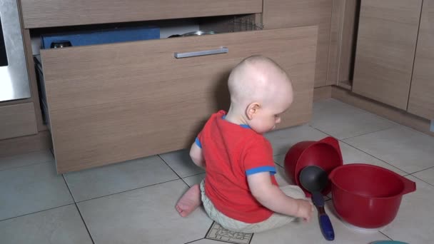 Baby boy doing mess in kitchen. Child play with bowls and utensil — Stockvideo