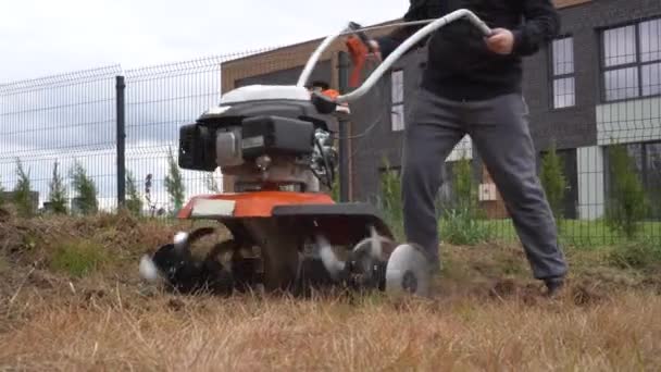 Zahradník uvolňuje půdu s chodícím traktorem v záhonech městských květin. Gimbalový pohyb — Stock video