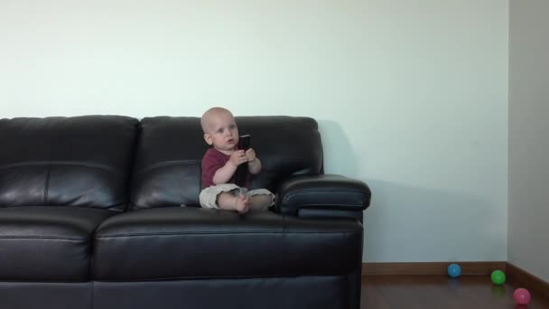 Lustiger Baby-Junge sitzt auf Sofa mit Fernbedienung — Stockvideo