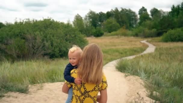 Jonge moeder vasthouden handen peuter zoon en lopen in de richting van zee strand — Stockvideo
