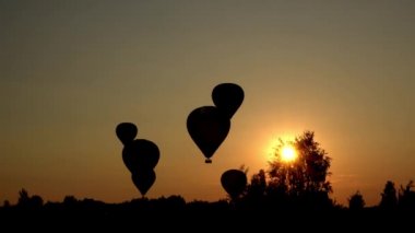 Sıcak hava balonlarının siluetleri muhteşem günbatımının üzerine iniyor. Güneş ışınları nüfuz ediyor