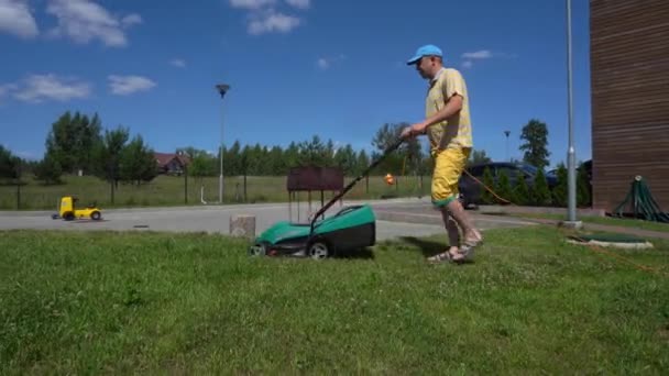 Homme travailleur tonds pelouse arrière-cour avec machine de tondeuse. Chaises de table et grill — Video