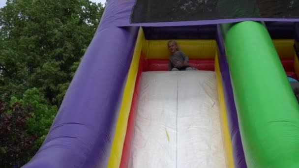 Verspielte Mädchen rutschen auf aufblasbarem Spielplatz-Trampolin hinunter. Gimbal-Nachschuss — Stockvideo