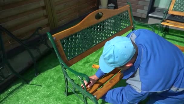 Foreman in blue connect parts of wooden bench in house yard — Stock Video