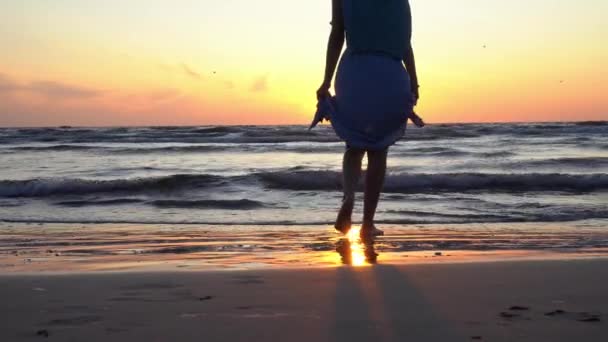 Meisje houden jurk en lopen blootsvoets op natte zee kust zand bij zonsondergang — Stockvideo