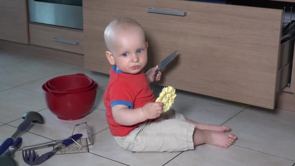 Menino come comida sentada na bagunça no chão da cozinha — Vídeo de Stock