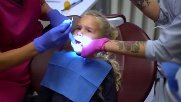Tandläkare och hennes assistent med tatuerade händer reparera små flicka barn tänder — Stockvideo