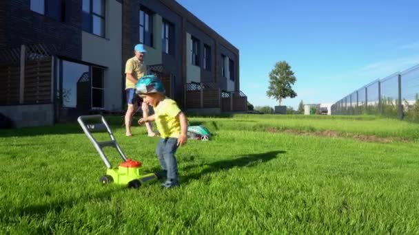 Padre cortando césped con cortacésped mientras el hijo juega con cortacésped de juguete. Movimiento del cardán — Vídeo de stock