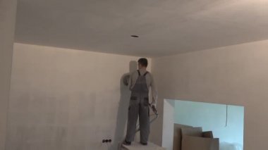 Yeni apartman dairesinde öğütücü makineli bir adam duvar boyuyor.