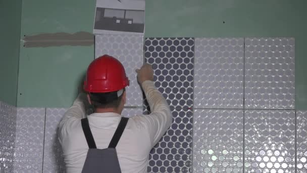 Geschoolde arbeider met beschermende helm leggen tegels op de muur — Stockvideo