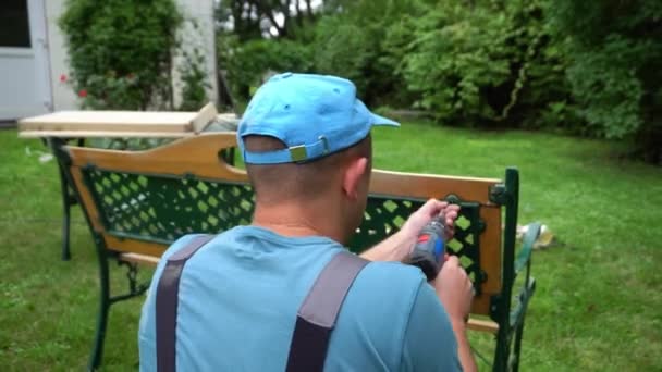 Carpenter guy with screwdriver disassemble retro bench. Outdoor furniture — 비디오