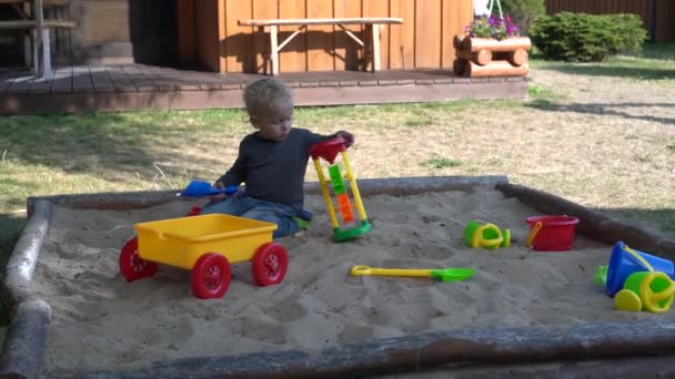 Ενθουσιασμένο αγοράκι που παίζει με πολύχρωμα παιχνίδια σε αμμόλοφο το καλοκαίρι — Αρχείο Βίντεο