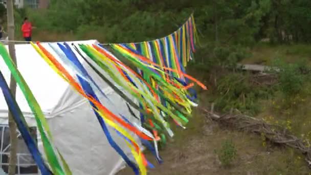 Красочные украшения гирлянды висят возле палатки для вечеринок и людей, гуляющих на природе — стоковое видео