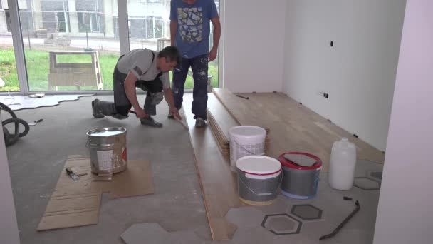 Werknemers met vuile kleding leggen parketvloer planken in de woonkamer — Stockvideo