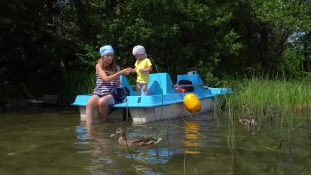 Женщина с маленьким мальчиком кормит уток на катамаране возле дикого озера — стоковое видео