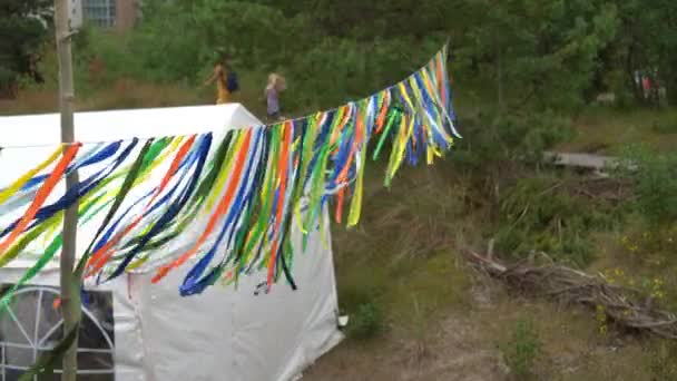 Färgglada band hänga nära partytält och människor vandrar i naturen — Stockvideo