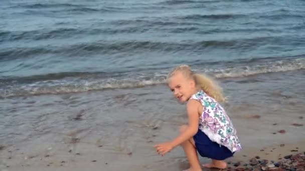 Chica jugando con piedras mojadas en la costa. Niño lavándose las manos en olas — Vídeos de Stock