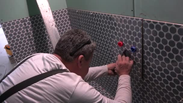 Квалифицированный работник делает отметки на плитке, чтобы увеличить отверстия вокруг водопроводов — стоковое видео