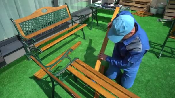 男は屋外の庭に家具のベンチを組み立てる。カメラの動き — ストック動画