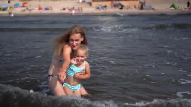 Mulher e filha brincalhão de frente para as ondas do mar. meninas emocionais obter água salpicada — Vídeo de Stock