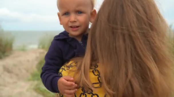 Мать несет сына на руках к морскому пляжу — стоковое видео