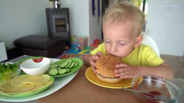 Criança europeia branca comendo hambúrguer grande saboroso com grande apetite. Movimento de Gimbal — Vídeo de Stock