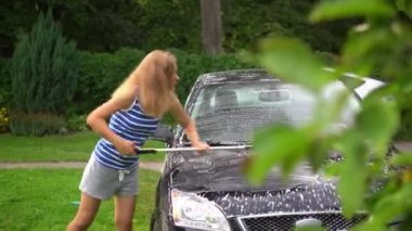 Young woman washing her soapy foamy car with brush tool