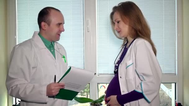 Врач-мужчина дает своей коллеге беременную женщину подписать документы — стоковое видео