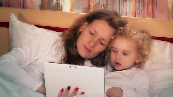 Νεαρή γυναίκα και αξιολάτρευτο κοριτσάκι χρησιμοποιώντας το tablet pc κάθεται στο κρεβάτι — Αρχείο Βίντεο