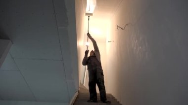 Boyacı merdiven tavanını tekerlekli araçla boyuyor.