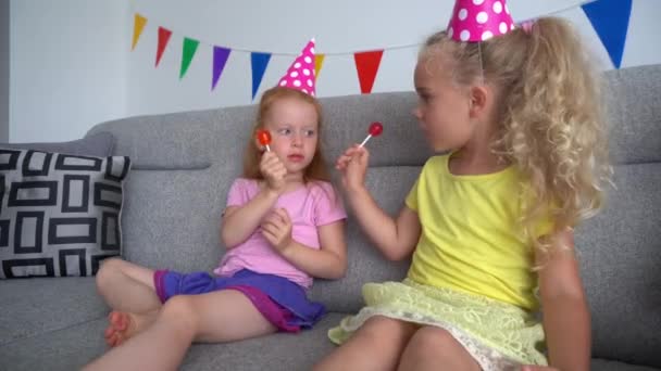 Mejor amigo niñas jugar con dulces caramelos en palos y ver televisión sentado — Vídeos de Stock
