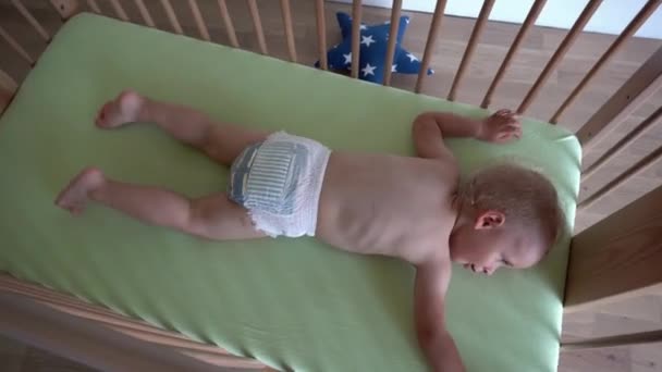 Niño activo en pañales acostado en una cama de madera. Movimiento de cardán — Vídeos de Stock